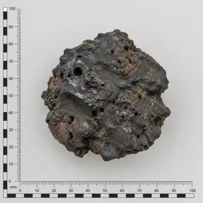 Customer specimen 08: glassy black lumpy fragment, photographed beside a millimeter scale